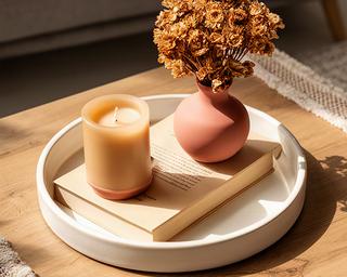Mesa de centro con bandeja de cerámica, vela artesanal, libro de tapa dura y un pequeño jarrón con flores secas