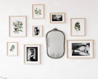 Galería de cuadros con marcos de madera clara sobre pared blanca, combinando ilustraciones botánicas y fotografía en blanco y negro